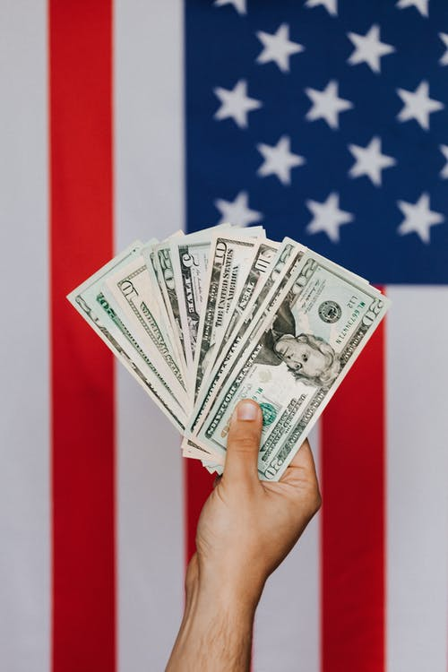 a person holding dollar notes in front of the American flag